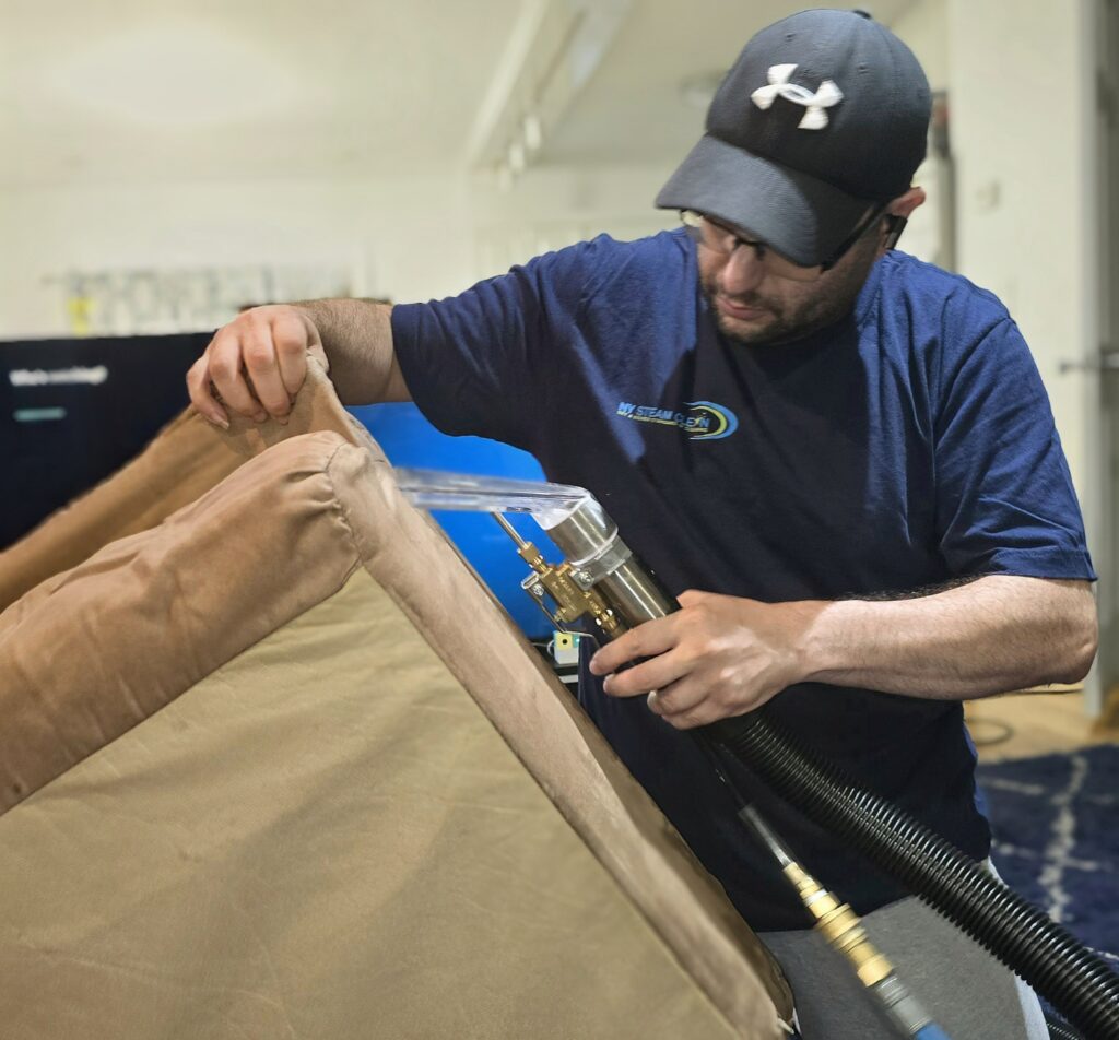 man with NY Steam Logo cleaning a couch cusjion